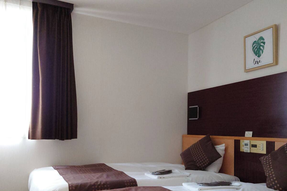 A hotel room with two beds, a large window with curtains, a wall-mounted TV, and a framed picture with the word "Love".