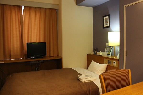 A hotel room with a bed, a television on a desk, a lamp, and a framed picture on the wall.