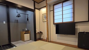 Une pièce de style japonais traditionnel, avec un sol recouvert de tatamis, une télévision et un petit meuble en bois.
