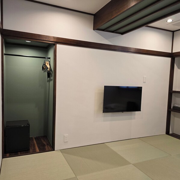 A room with a flat-screen TV mounted on the wall, a small black speaker, and a wooden floor.