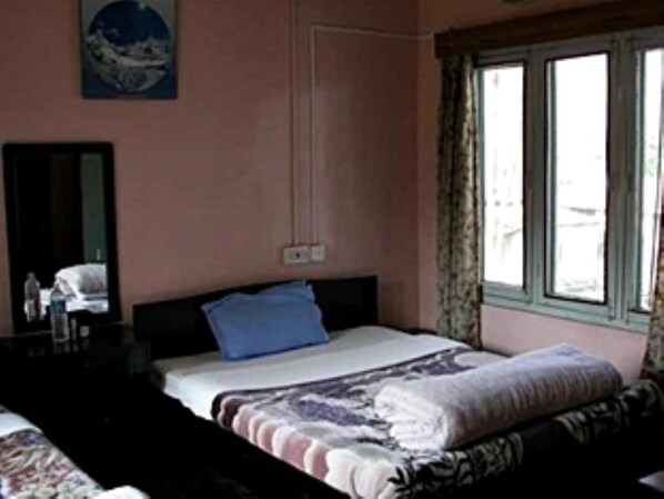 A bedroom with a single bed, a dresser, a mirror, and a window with curtains. - Rhino Lodge & Hotel (Sauraha)