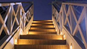 Una escalera de madera con barandilla, iluminada por luces en la pared.