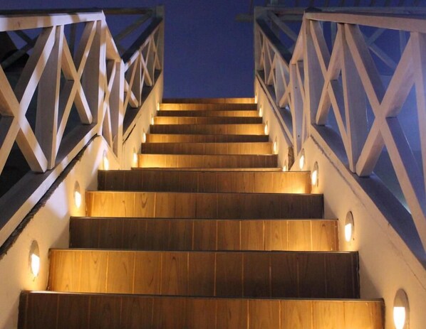 A wooden staircase with a railing, illuminated by wall-mounted lights. - Hotel Dorado Plaza Punta Arena (Cartagena)