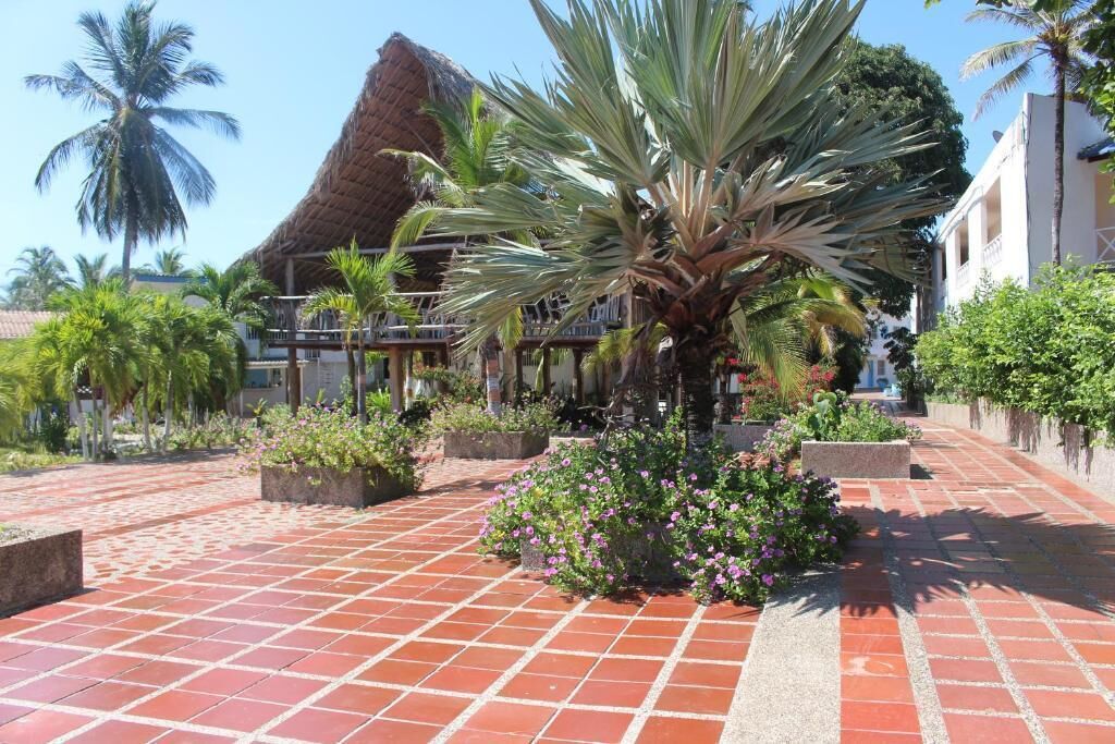 A courtyard with a thatched-roof building, palm trees, and a paved walkway.