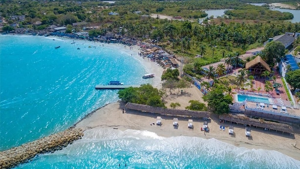 Vista aérea de un complejo turístico con piscina, sombrillas de playa y un litoral rocoso.
