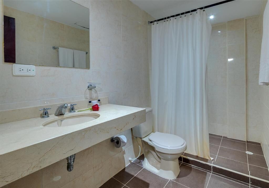 Ein Badezimmer mit Marmorwaschbecken, Toilette, Duschvorhang und Spiegel.