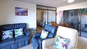 A living room with a blue sofa and a white armchair, both with butterfly-patterned cushions. A painting of a sailboat is on the wall. - Marcel Towers Holiday Apartments (Nambucca Heads)