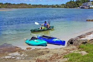 Un kayakista en un lago tranquilo, con dos kayaks en la orilla.