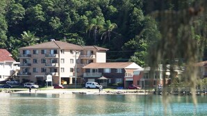 A multi-story building with balconies, a parking area, and a body of water in the foreground. - Marcel Towers Holiday Apartments (Nambucca Heads)