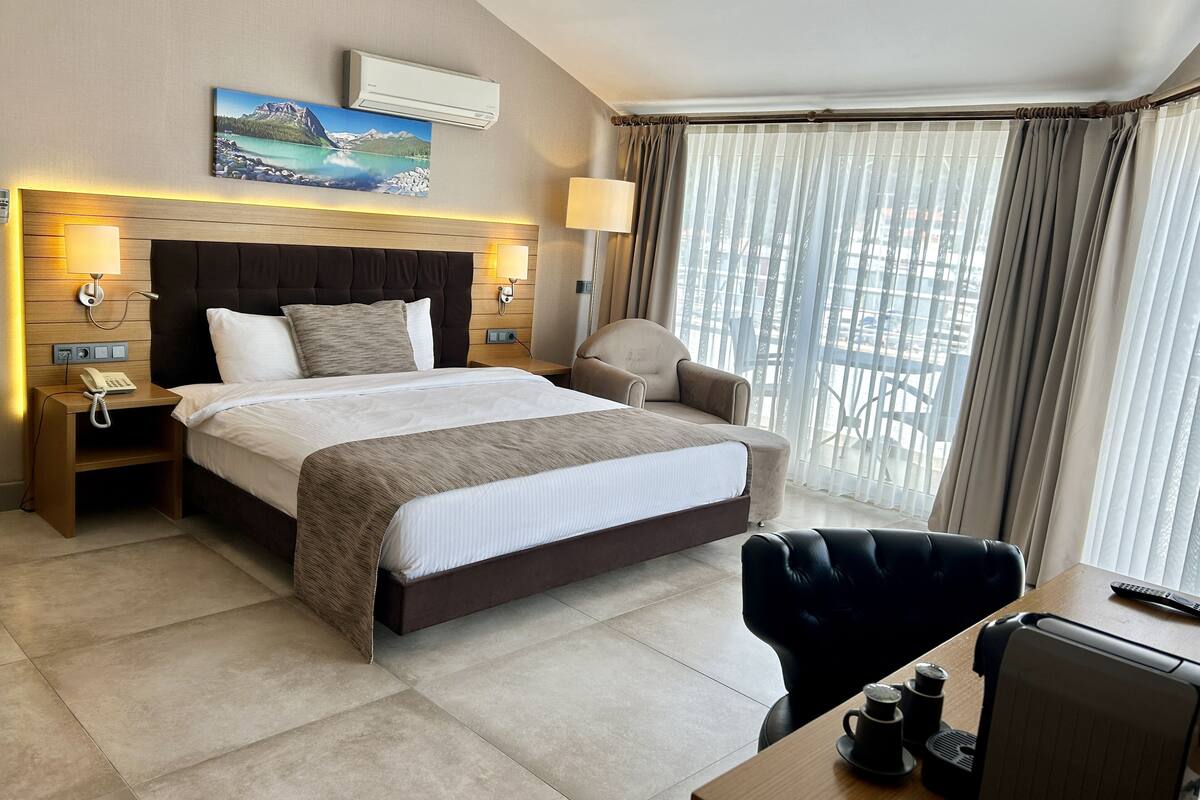 A hotel room with a large bed, bedside tables, a desk, a chair, and a window with curtains.