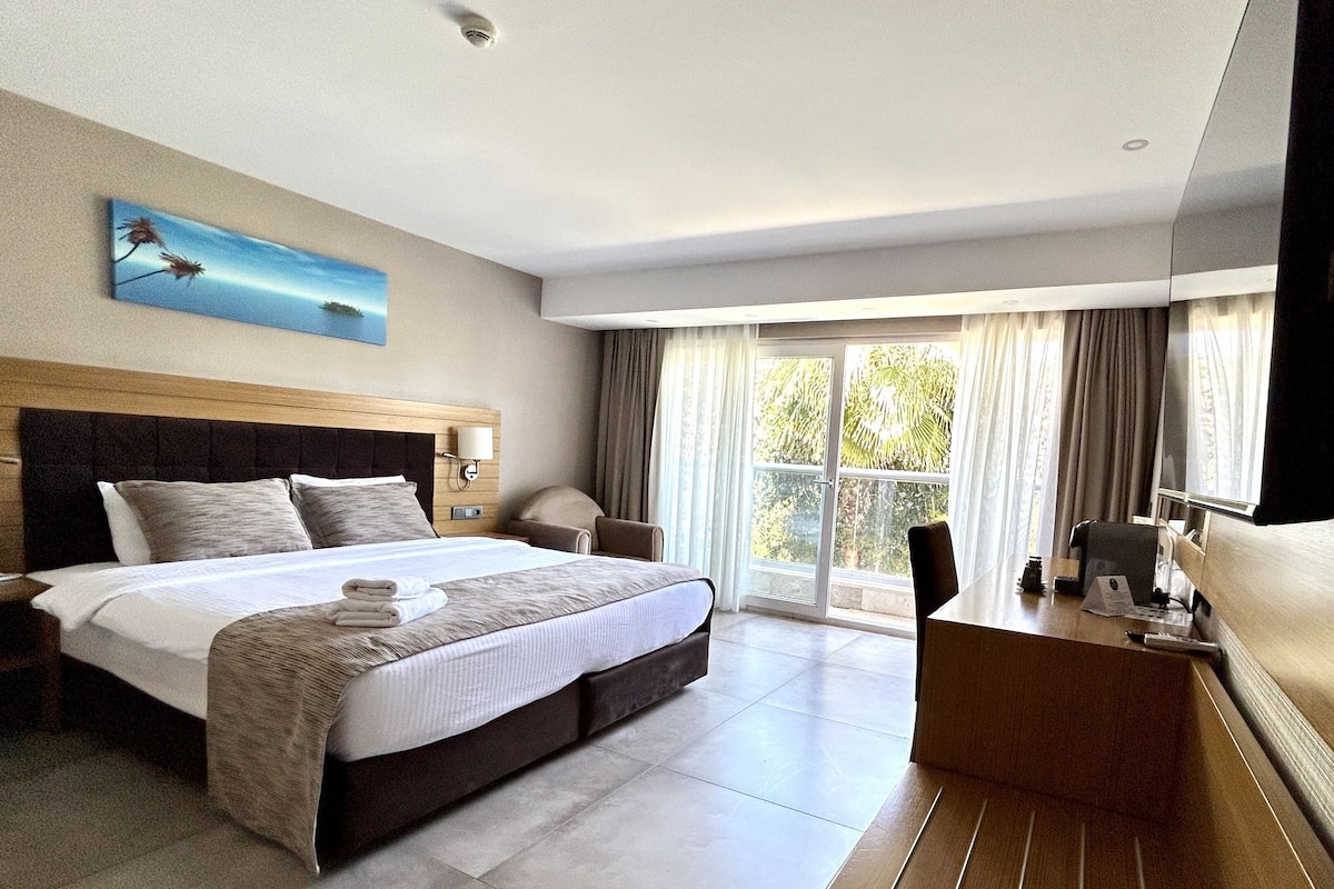 A hotel room with a large bed, a desk, and a view of the outdoors.