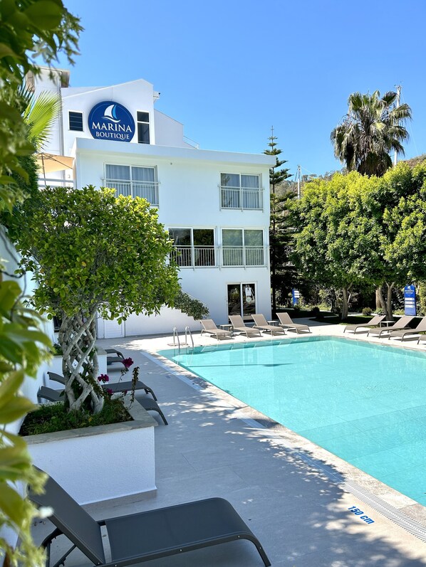 A white building with a sign reading "MARINA BOUTIQUE" and a swimming pool with lounge chairs. - Marina Boutique Fethiye - Boutique Class (Fethiye)