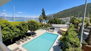 A pool area with lounge chairs, a clear blue pool, and a view of boats and hills in the background. - Marina Boutique Fethiye - Boutique Class (Fethiye)