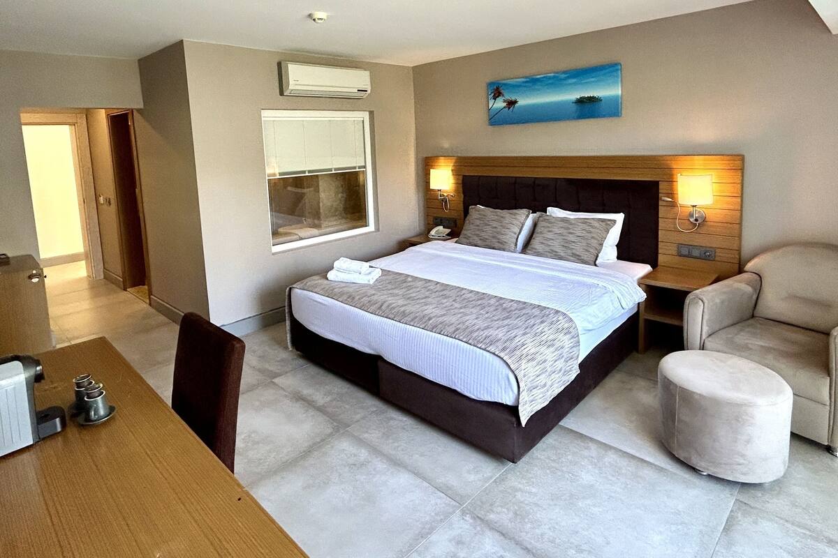 A hotel room with a bed, bedside tables, a chair, a desk, and a painting on the wall.
