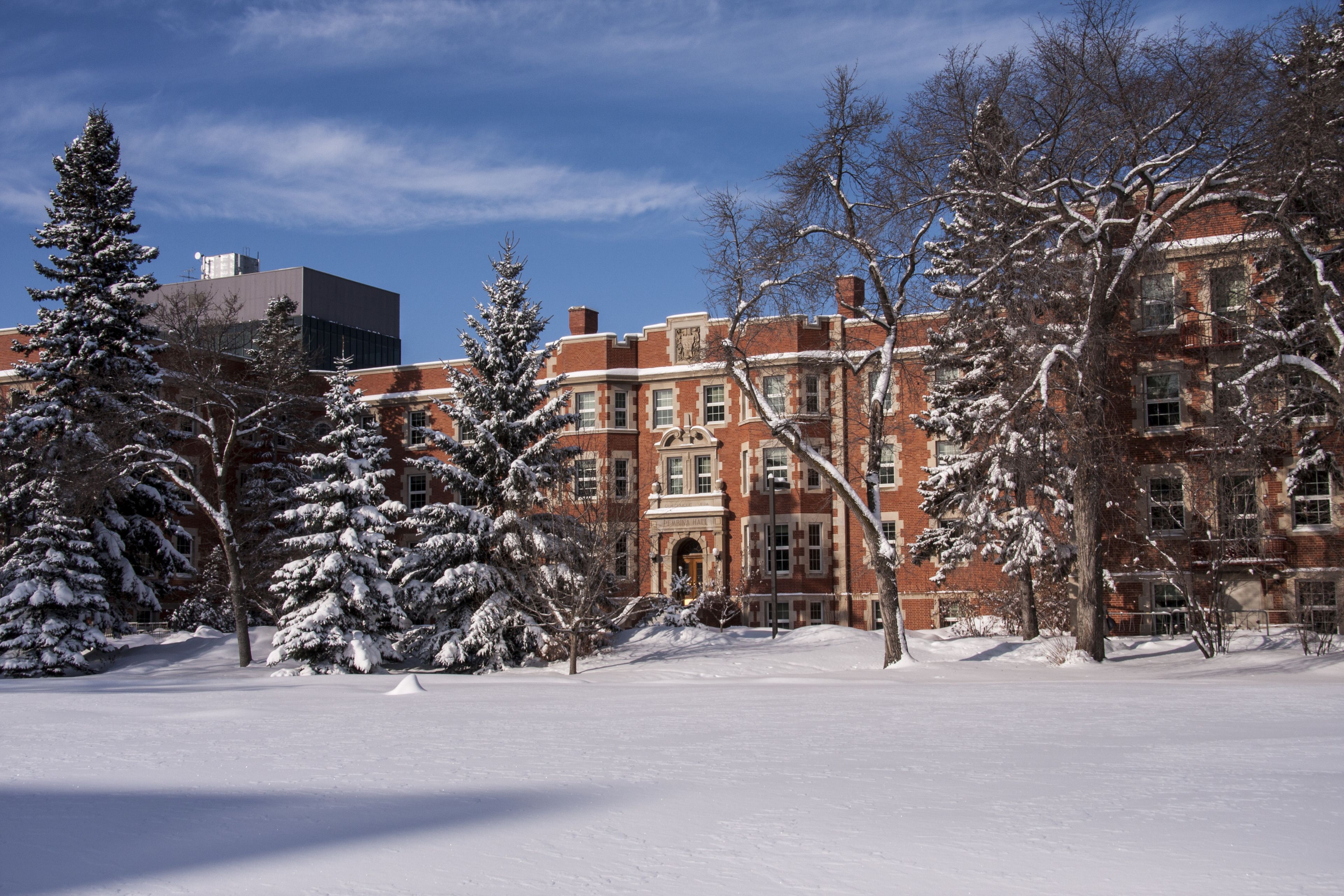 A snow-covered campus with a prominent red brick building, snow-laden trees, and a clear blue sky.
