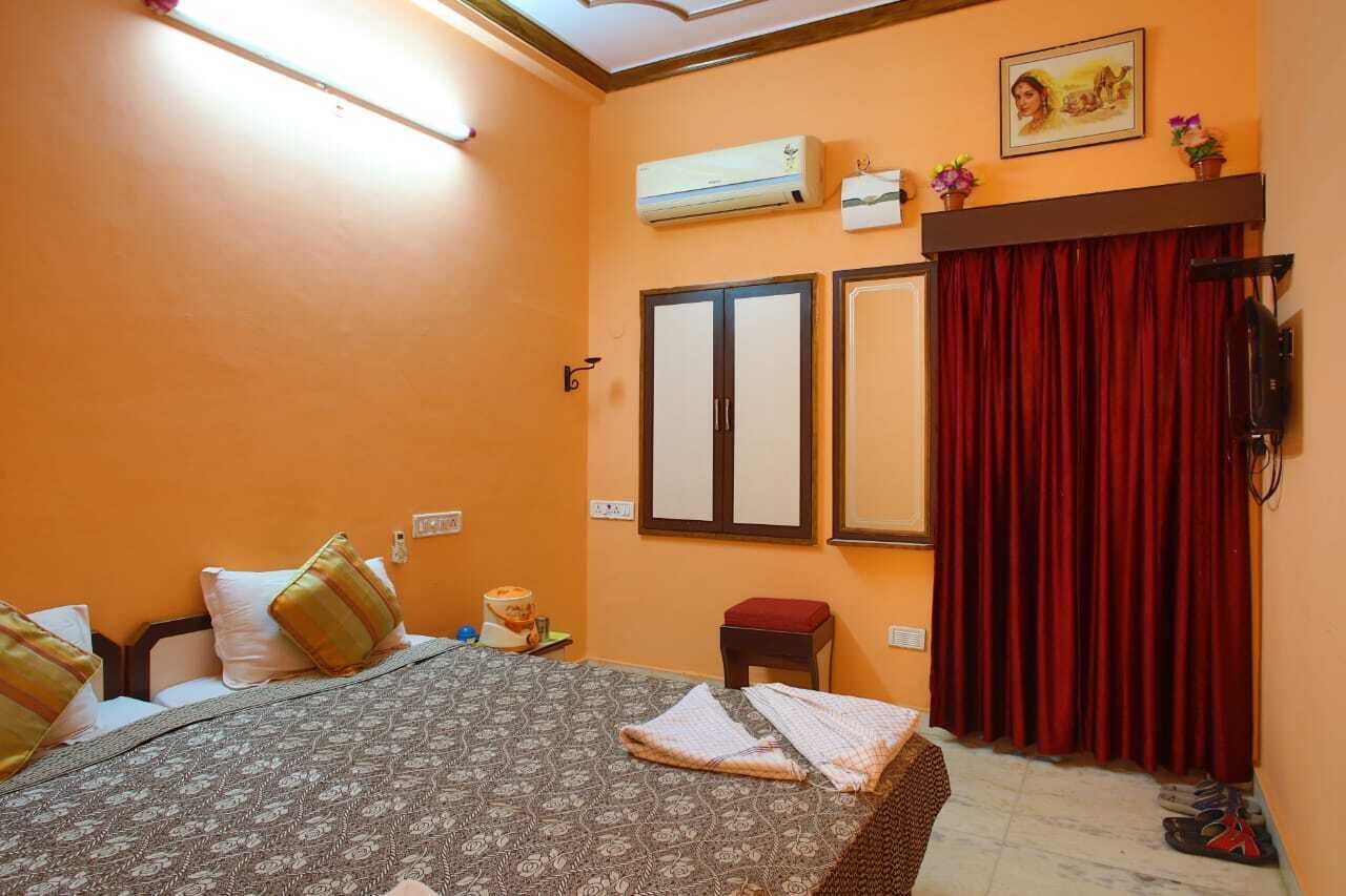 A hotel room with a bed, a small table, an air conditioner, a mirror, and a red curtain.