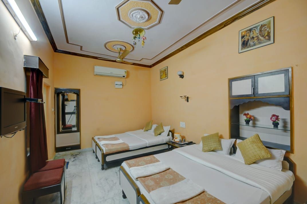 Habitación de hotel con dos camas, ventilador de techo, aire acondicionado, televisión y espejo.