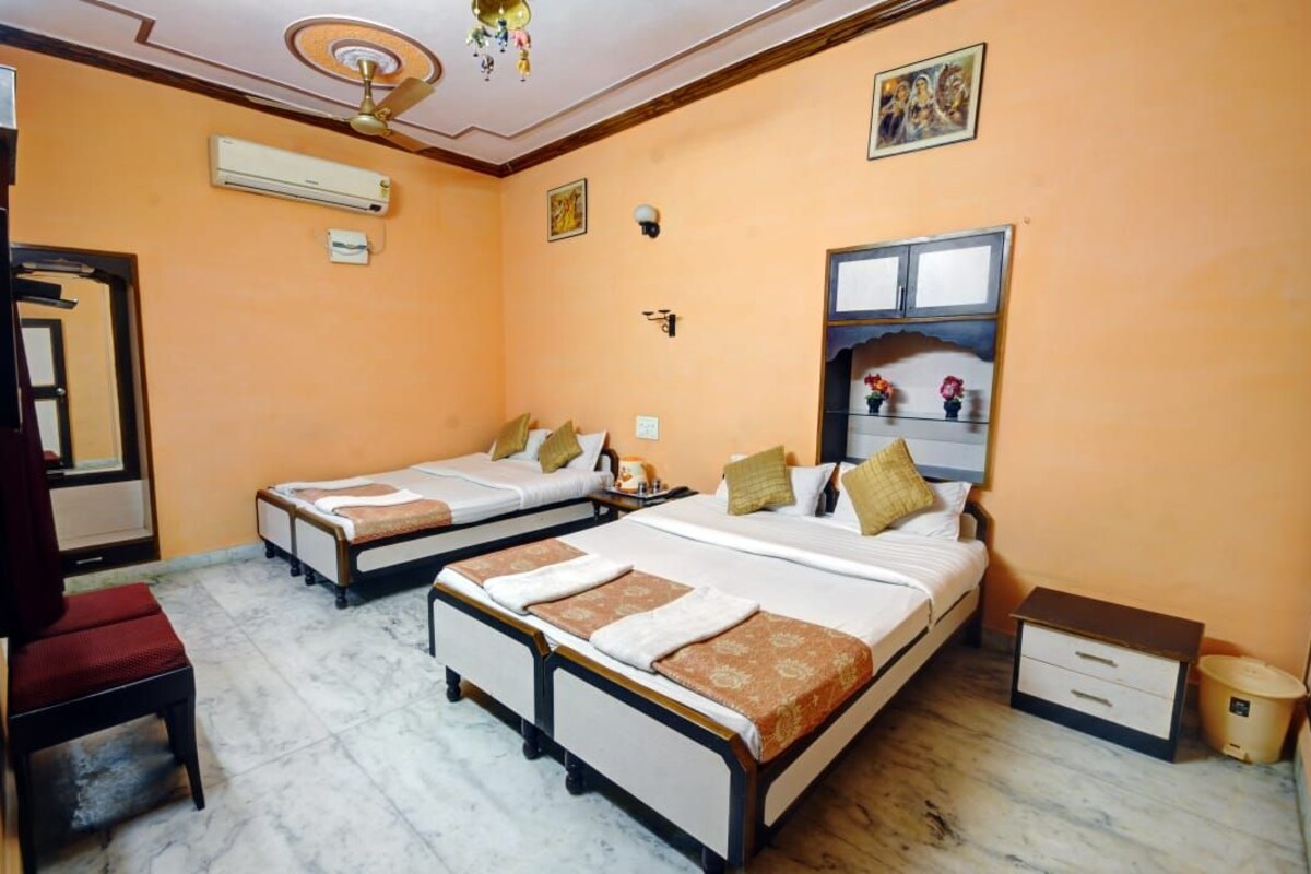 Une chambre d’hôtel avec deux lits simples, un bureau, une chaise, un climatiseur, un ventilateur de plafond et un petit placard.