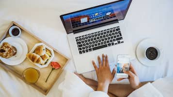 Een laptop op een bed, met een dienblad eten en drinken erop.