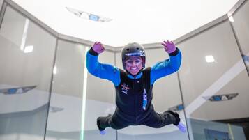 Eine Person in blauer und schwarzer Kleidung führt einen Sprung in einer modernen Indoor-Einrichtung mit Glaswänden und Deckenkonstruktionen aus.