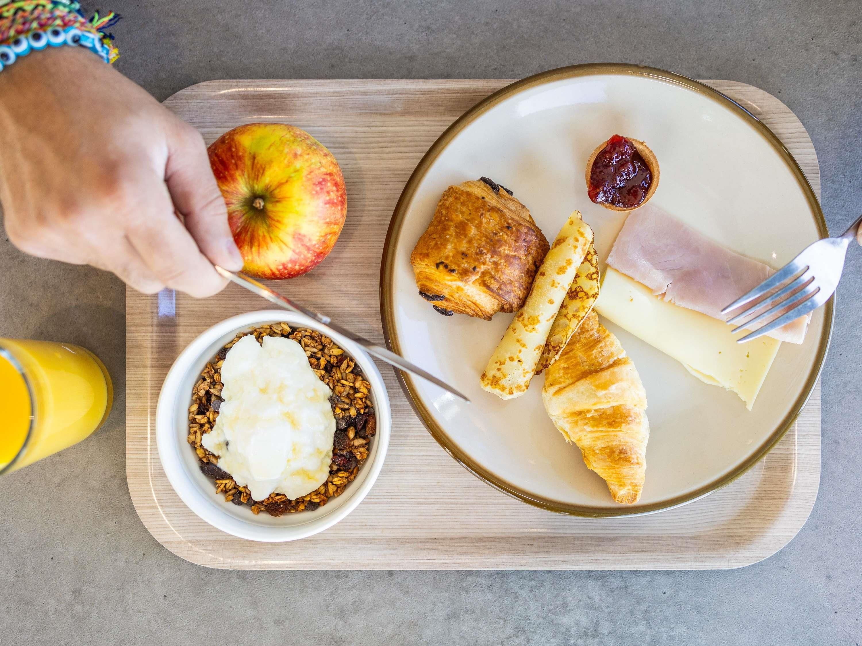 A breakfast tray with a croissant, ham, cheese, apple, and a bowl of yogurt with granola.