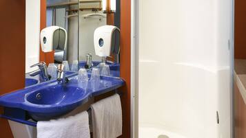 Un baño con un lavabo azul, un espejo, una toalla blanca y una cabina de ducha de vidrio.