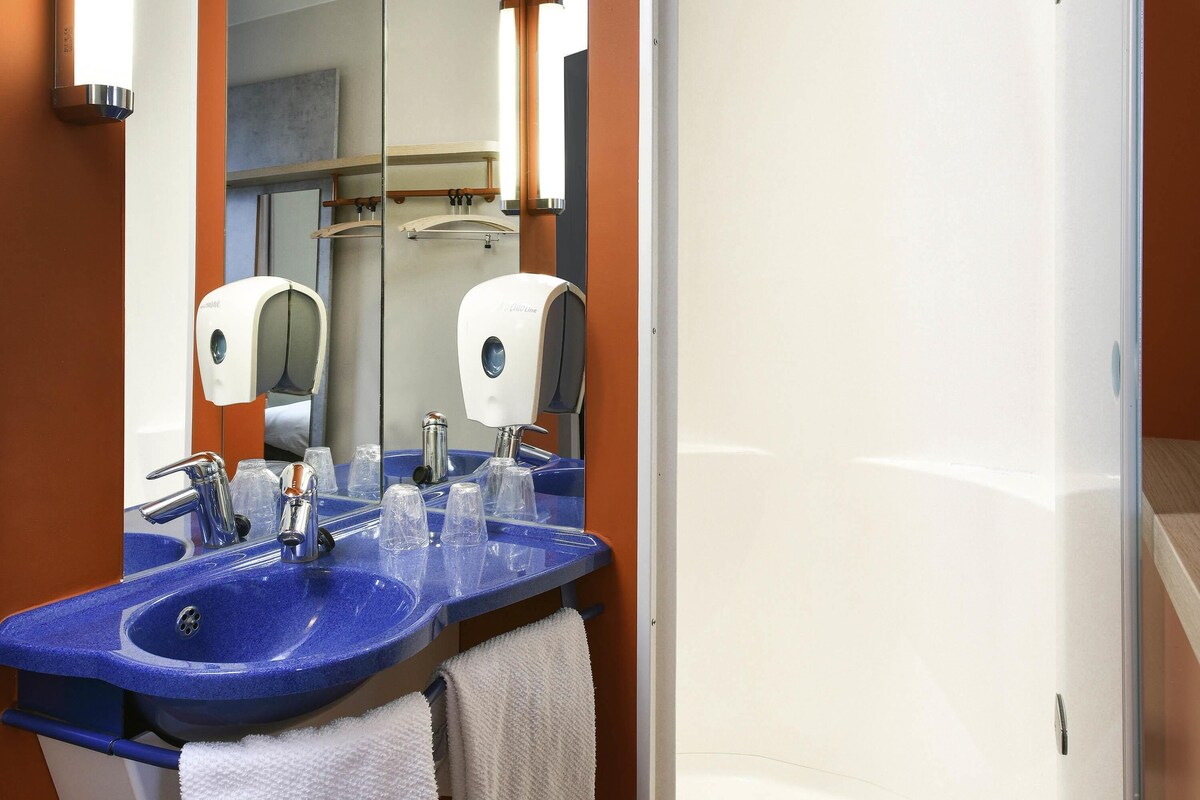 A bathroom with a blue sink, two paper towel dispensers, a mirror, and a white towel hanging on a rack.