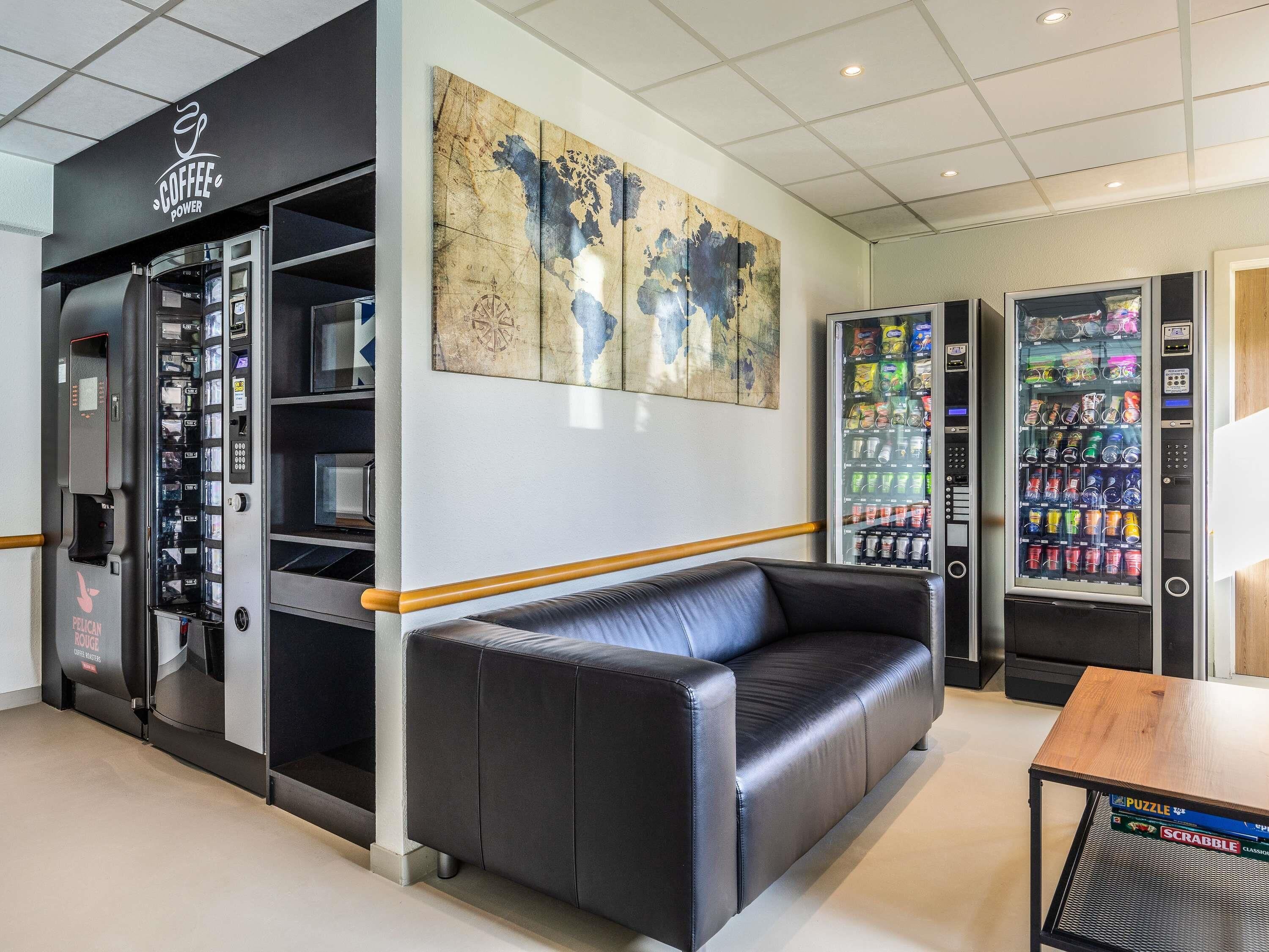 A modern interior with a coffee machine, vending machines, a leather couch, and a coffee shop sign.