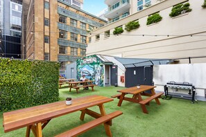 An outdoor patio with wooden picnic tables, a barbecue grill, and a mural on the wall. - Sydney Backpackers - Hostel (Sydney)