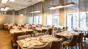 Un'ampia sala ristorante con numerosi tavoli apparecchiati, grandi finestre che lasciano entrare luce naturale e un arredamento dal design moderno.