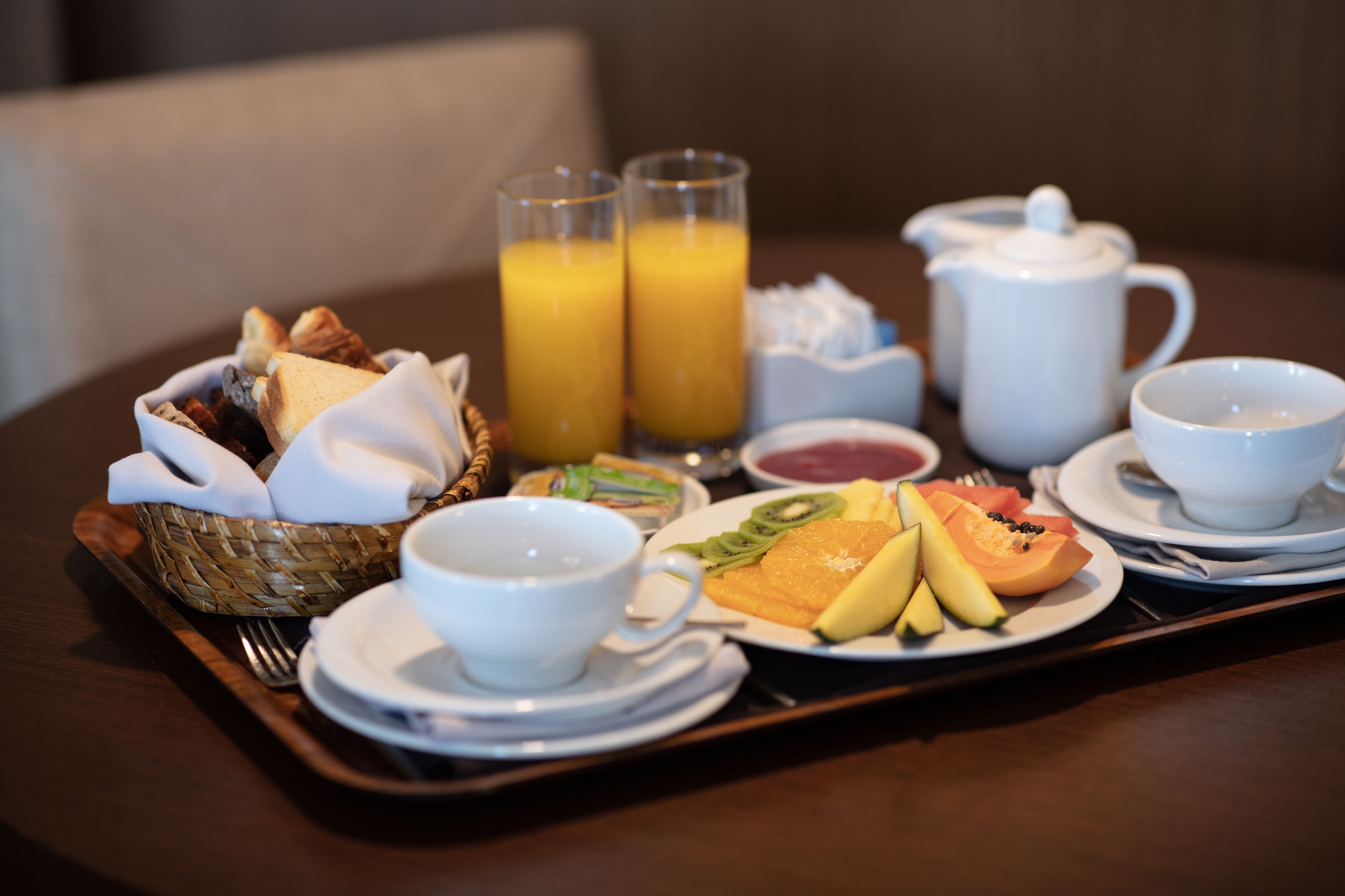 A breakfast tray with toast, fruit, juice, and tea on a wooden table.