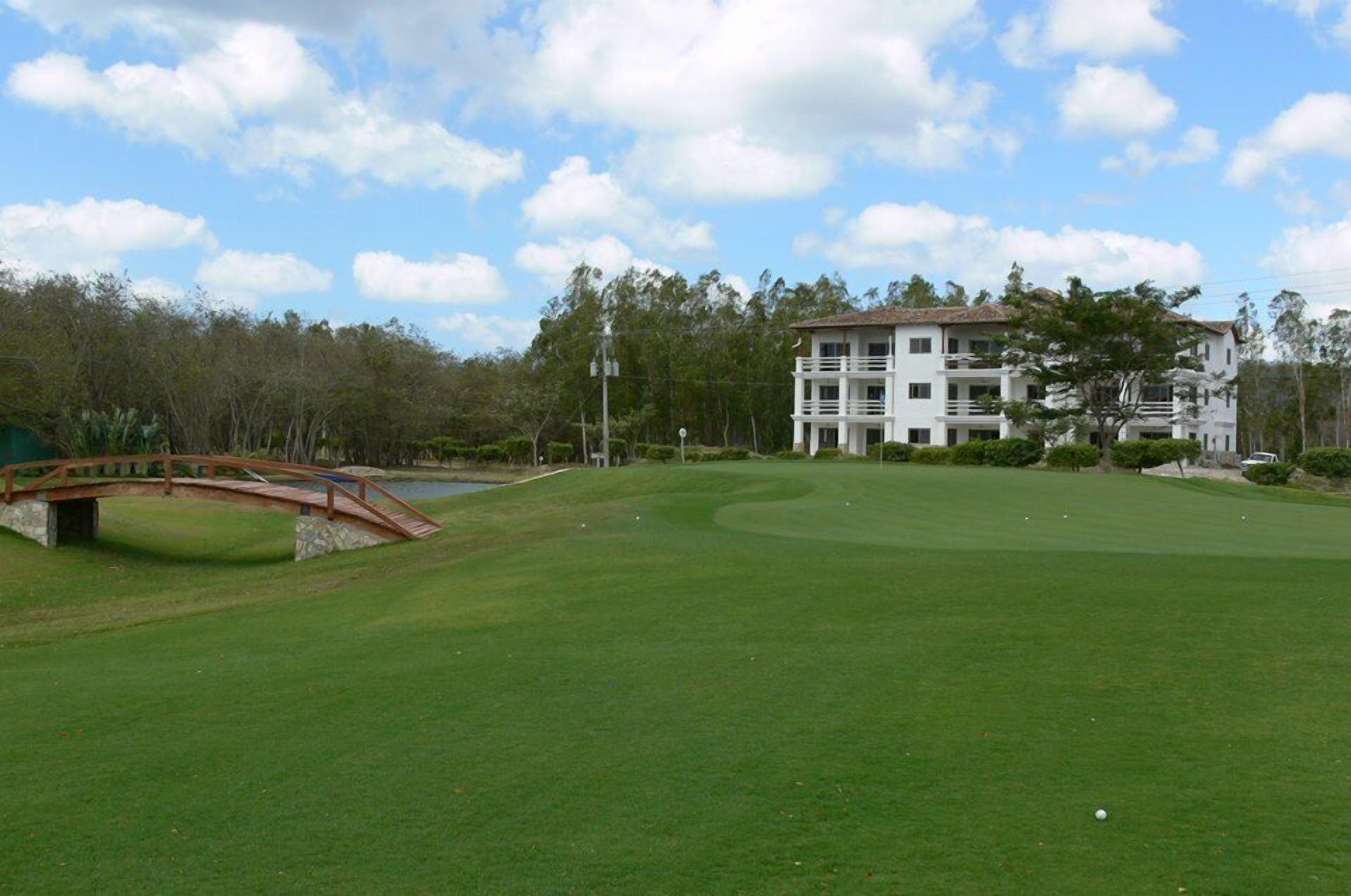 Un campo de golf con un puente, un estanque y un edificio al fondo.