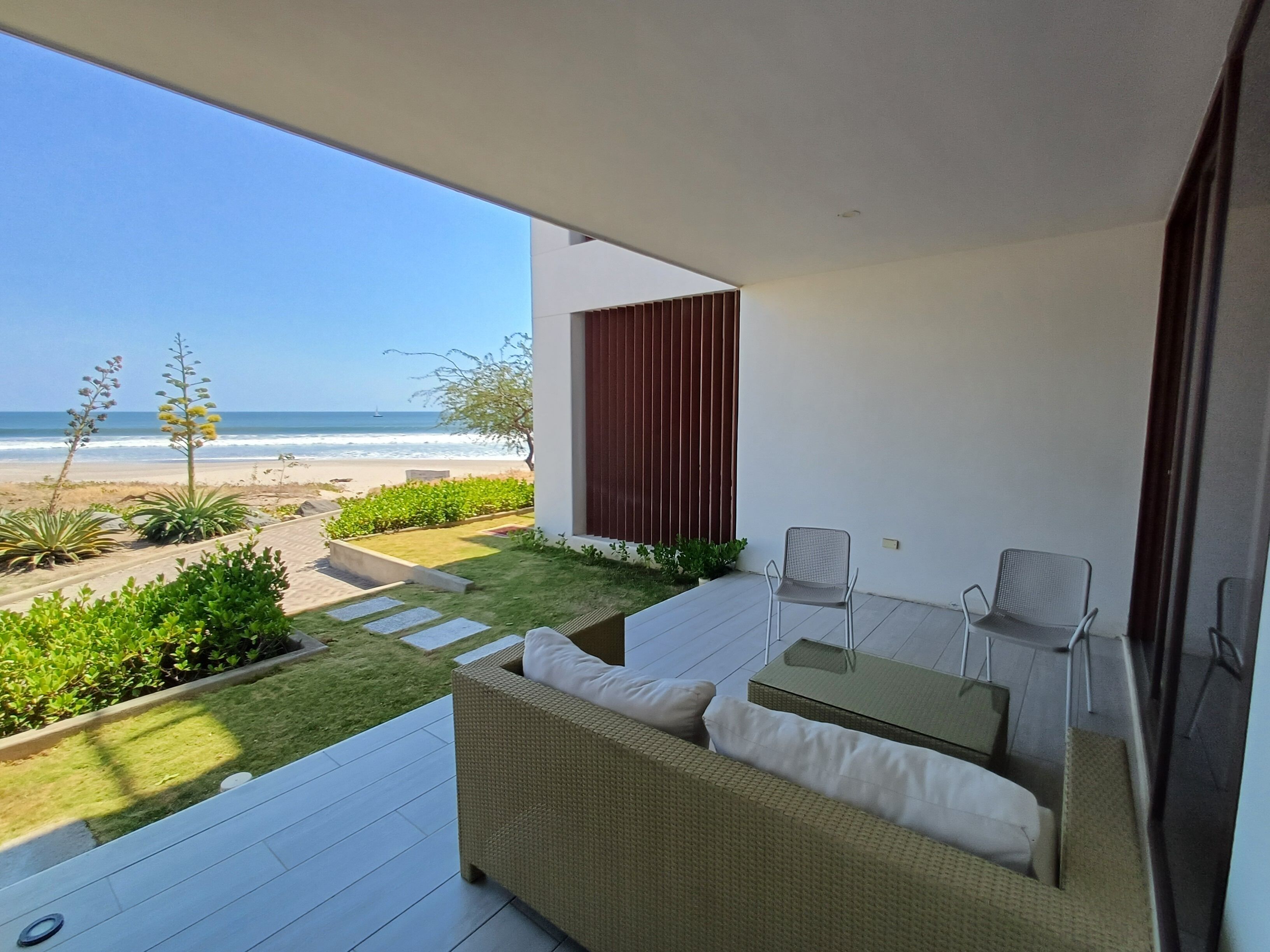 A balcony with a view of the beach, a wicker sofa, and a small table.