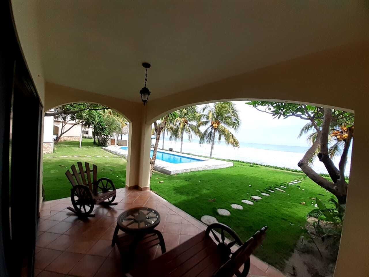 A covered outdoor area with a pool, palm trees, and a view of the ocean.
