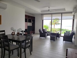 Amplia sala de estar con mesa de comedor, sillas y un juego de sofá. Un ventanal grande ofrece vistas del exterior.