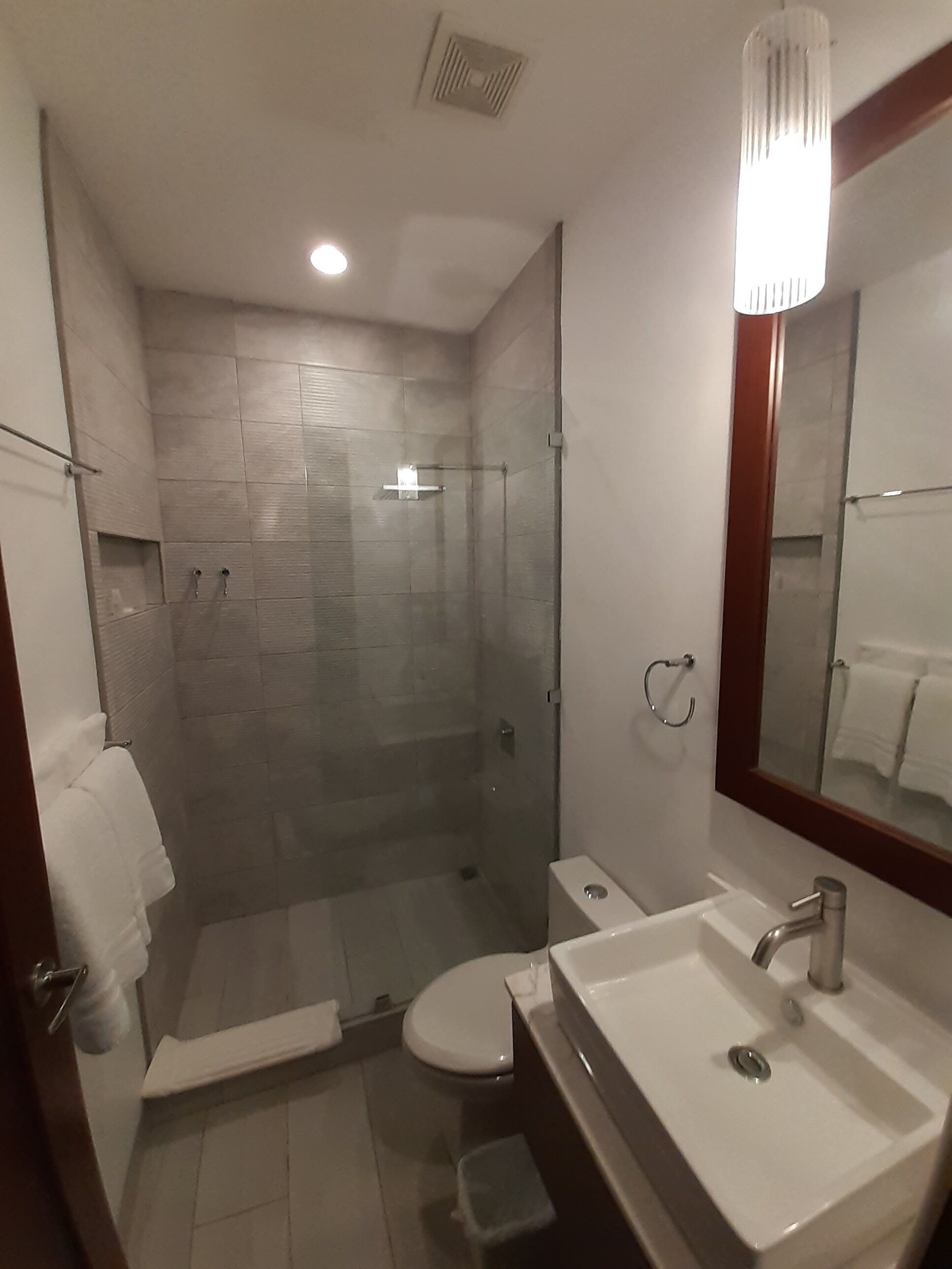 Un baño moderno con ducha de vidrio, inodoro y lavamanos con espejo.