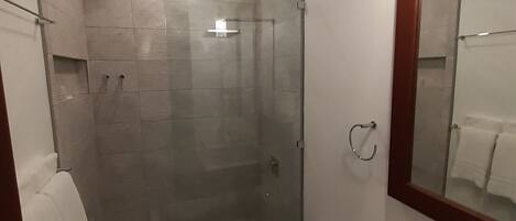 Un baño moderno con ducha de vidrio, inodoro y lavamanos con espejo.