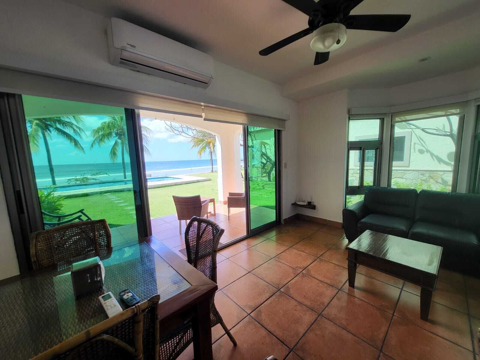 Una habitación con vista al mar, ventilador de techo, una mesa con sillas y un sofá.
