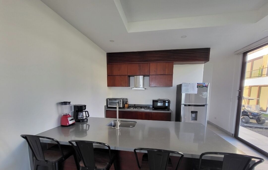 A modern kitchen with a dining table and chairs, a coffee maker, a toaster, and a refrigerator.