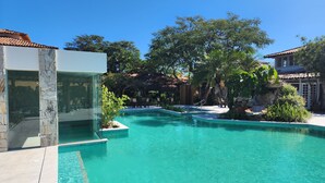 A swimming pool with clear blue water, surrounded by lush greenery and stone structures. - Pousada dos Tangaras (Búzios)