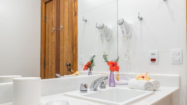 A bathroom with a white sink, two hair dryers mounted on the wall, a wooden door, and a mirror. - Pousada dos Tangaras (Búzios)