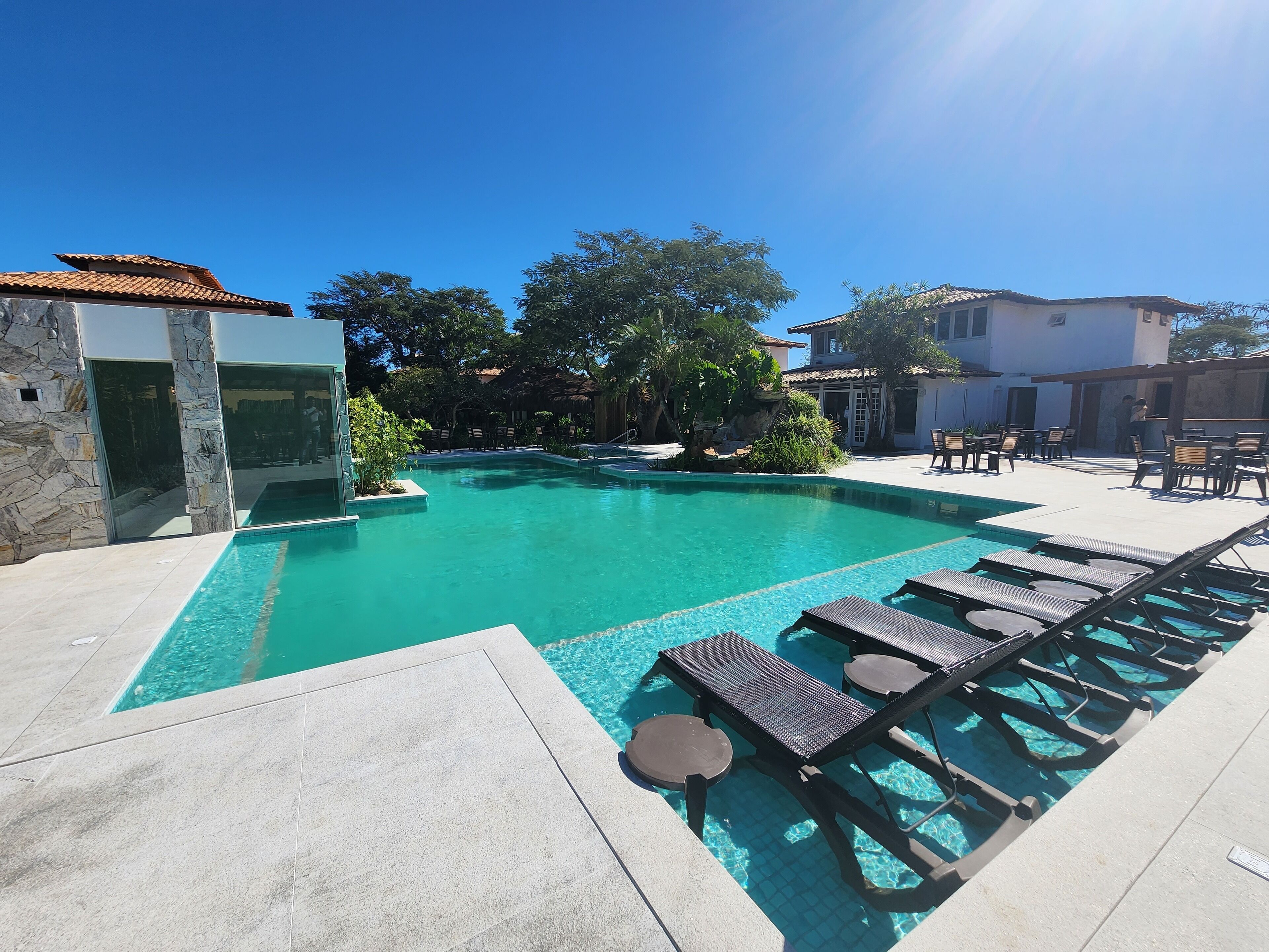 Een zwembad met ligbedden en een stenen muur.