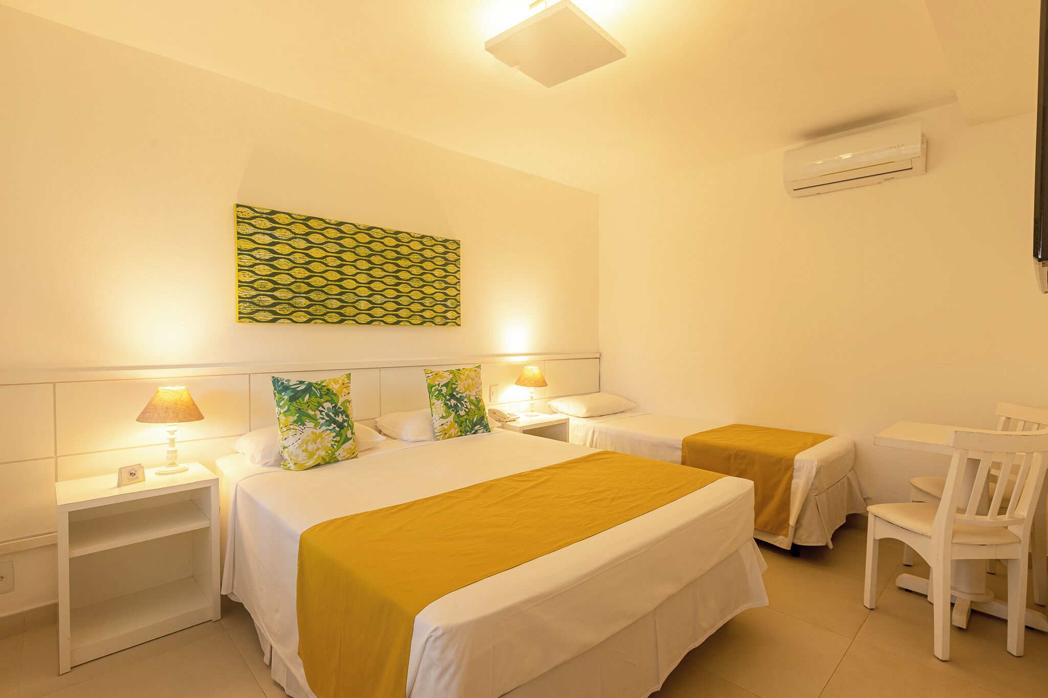 A hotel room with two beds, a desk, a chair, a wall-mounted air conditioner, and a patterned wall decoration.
