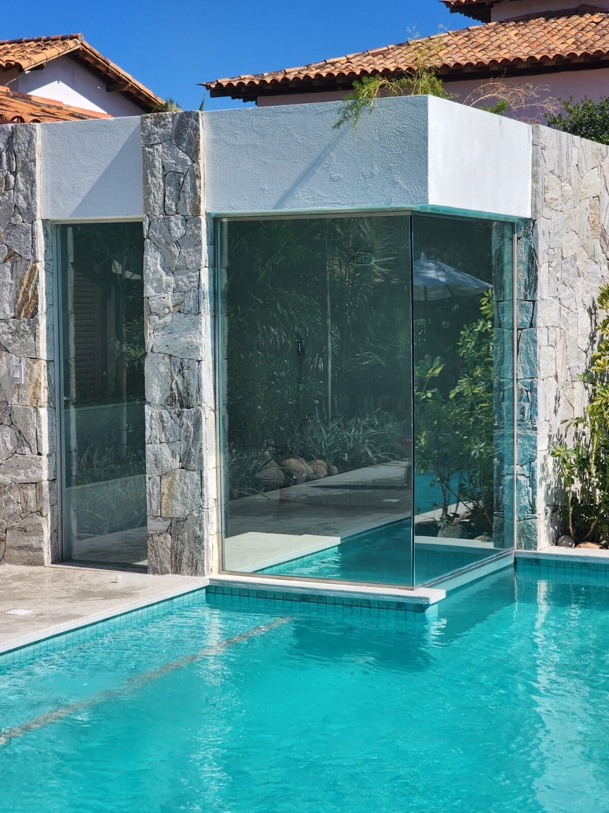 A modern pool area with stone walls and glass doors leading to a pool.