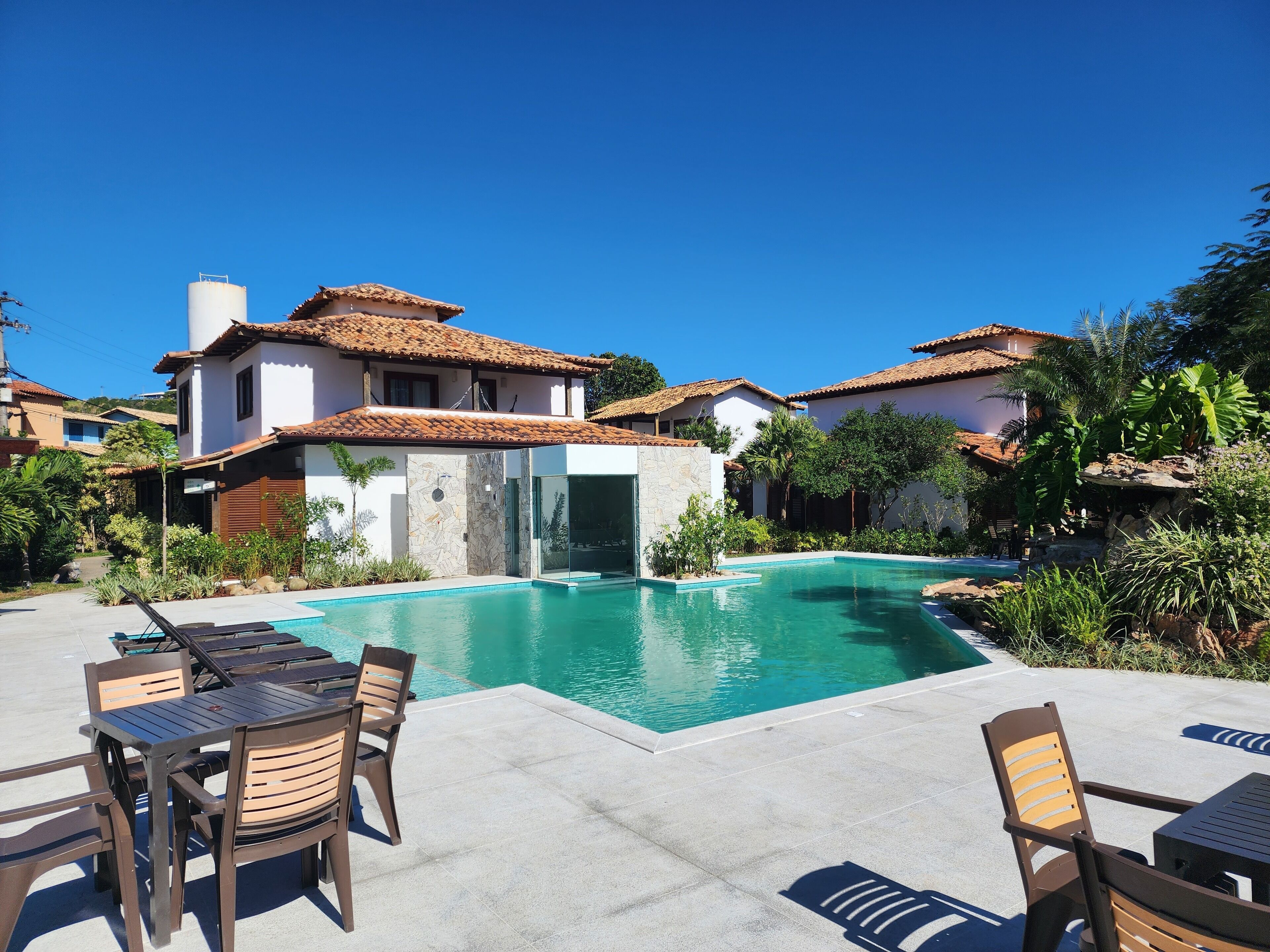 A pool area with a clear blue sky, a stone wall, and a table with chairs.