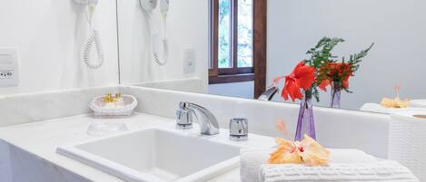 A bathroom with a white sink, a mirror, and a hairdryer mounted on the wall. There are towels and a vase with flowers on the counter.