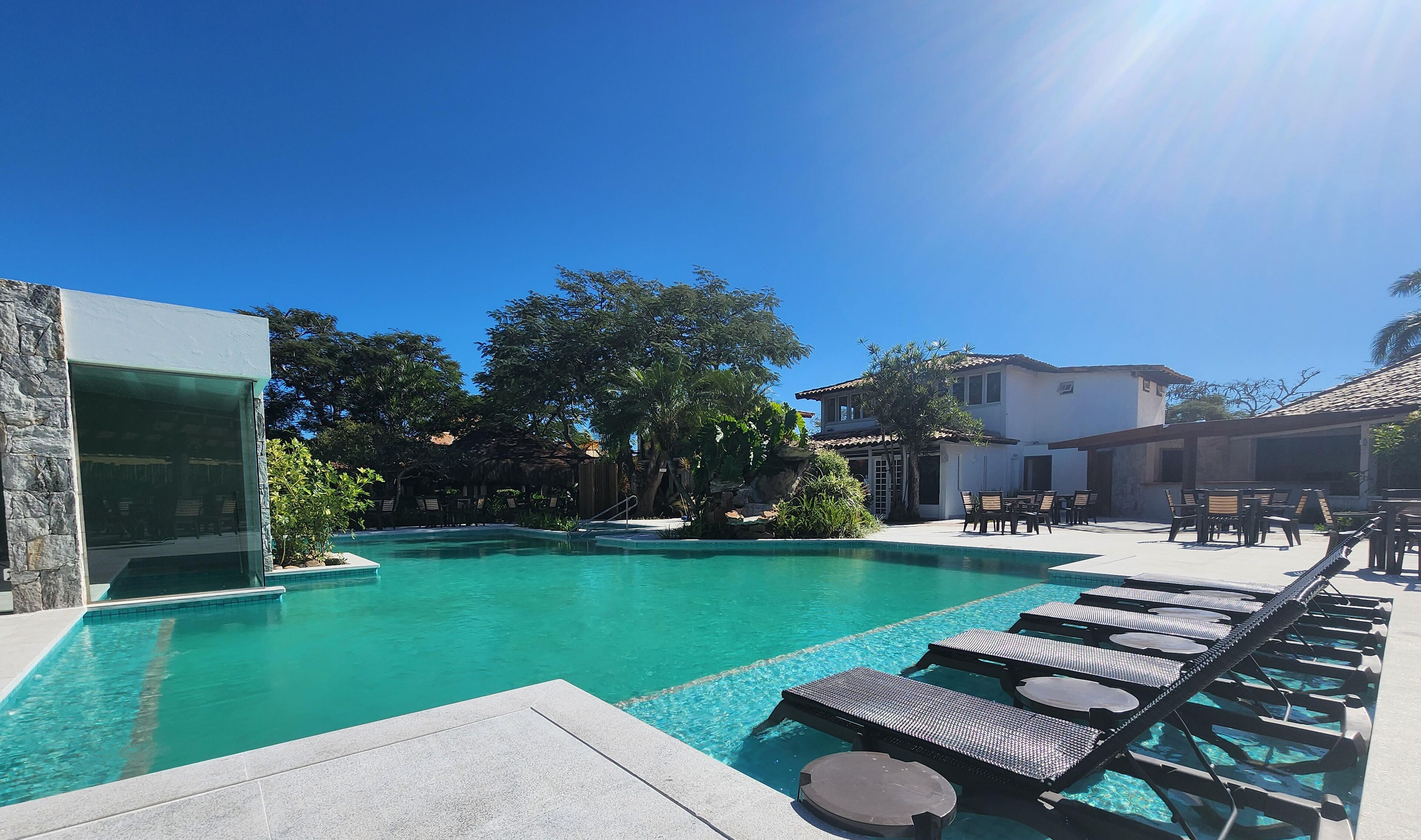 A pool area with lounge chairs, a stone wall, and a building with a tiled roof.