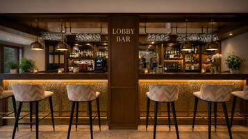 Angolo bar con un cartello che indica 'Lobby Bar', completo di sgabelli, un bancone con diverse bottiglie e bicchieri appesi.
