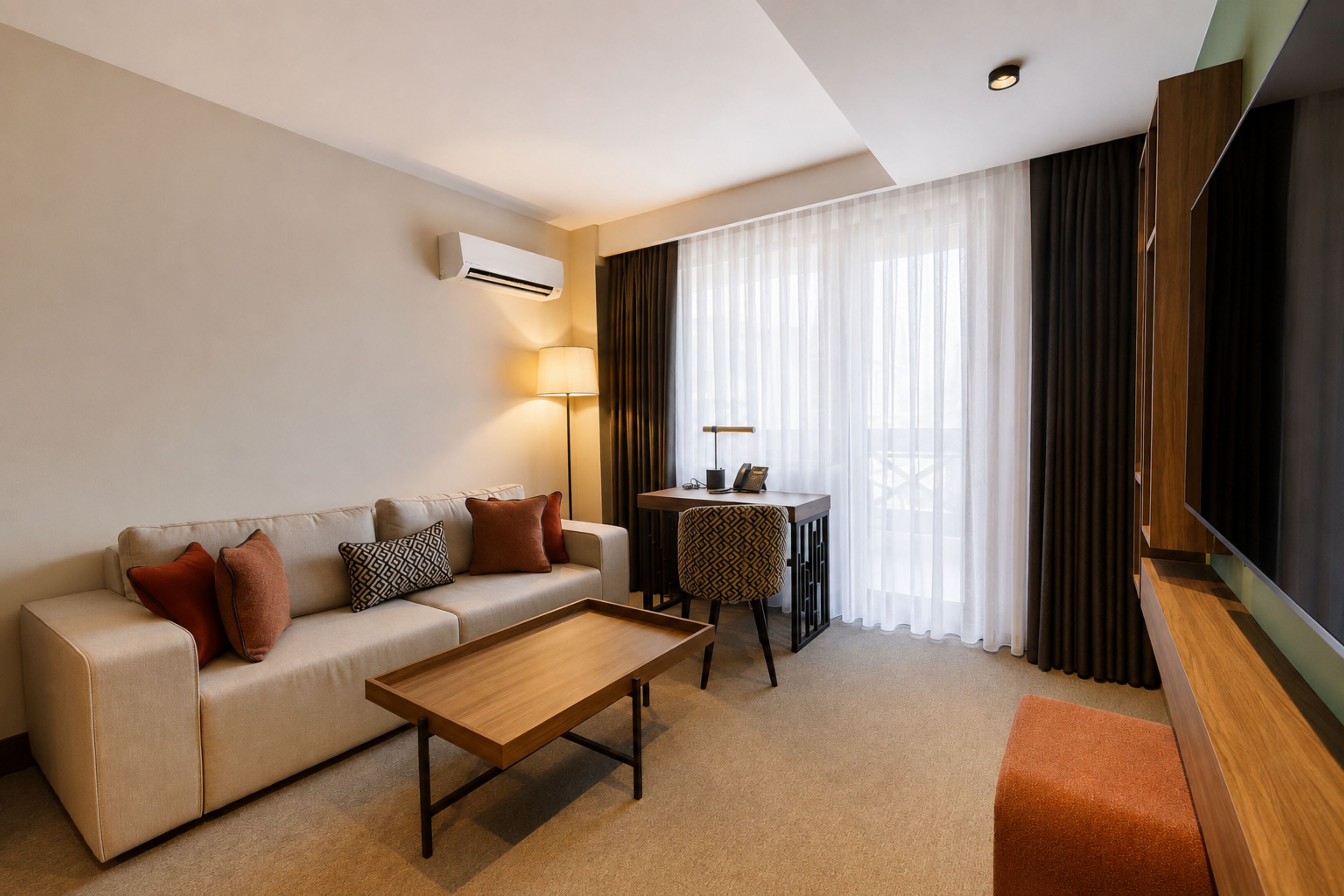 A modern hotel room with a sofa, a coffee table, a small side table, and a TV.