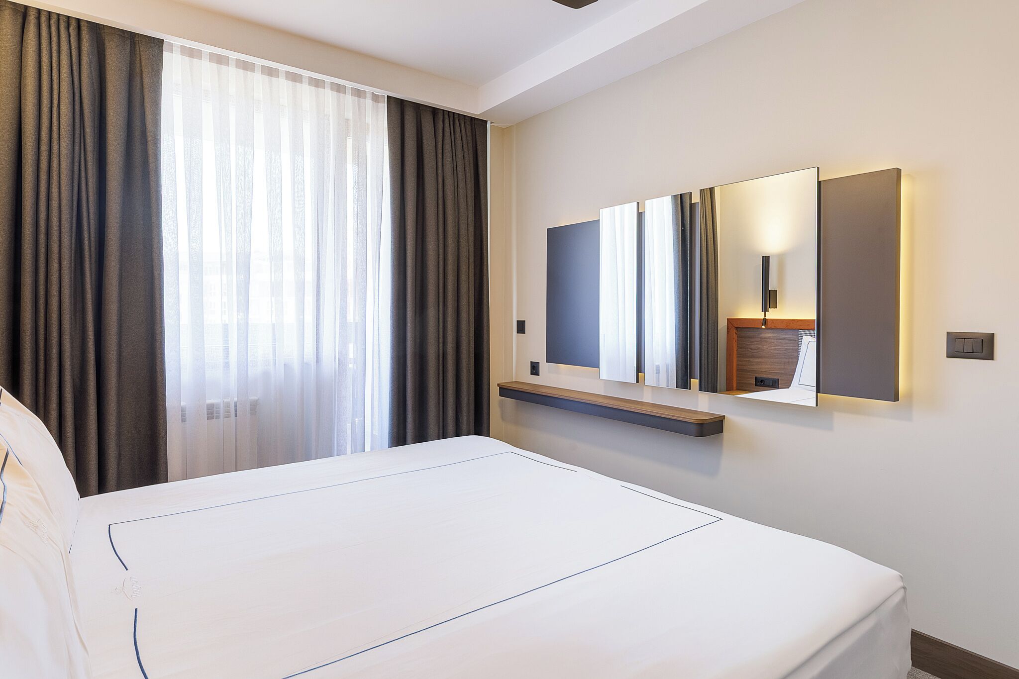 Habitación de hotel con una cama grande, una mesita de noche, un espejo y una ventana con cortinas.